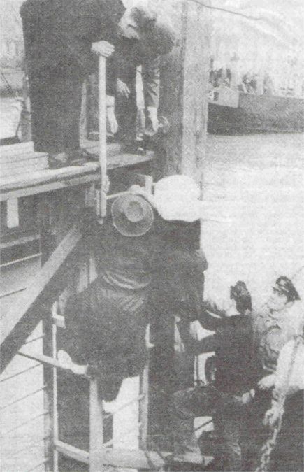 Het valt niet mee aan wal te komen. Behulpzame handen helpen deze vissersvrouw op de kade van de nieuwe thuishaven Colijnsplaat.