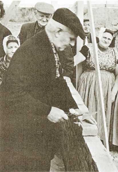 Het oudste lid van de Gereformeerde kerk, de 84-jarige P. Poortvliet, legt de eerste steen voor het nieuwe kerkgebouw. Rechts Janna Cornelisse- Schroevers.